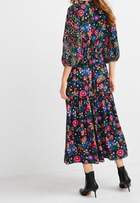 Robe maxi fleurie avec manches bouffantes, présentant un fond noir et des fleurs multicolores vives. Tissu lisse avec une silhouette à volants.