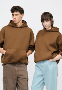 Rudi gobtuvu megzti džemperiai su priekinėmis kišenėmis, derinami su šviesiai mėlynomis kelnėmis. Atvaizduota ant vienspalvio balto fono.