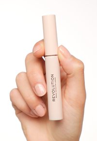 Un tube de gloss à lèvres de couleur rose clair, en forme cylindrique, tenu dans une main, avec un design épuré, sur lequel est inscrit "REVOLUTION" dans une teinte plus foncée.