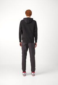 Felpa nera con cappuccio e maniche lunghe, pantaloni cargo grigi e sneakers rosse e bianche, vista dal retro. Design minimalista, senza motivi.