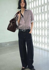 Camisa de cuadros, jeans amplios oscuros, bolsa de cuero y zapatos de punta. Las rayas son rojas y blancas; los jeans tienen detalles de costura en contraste.
