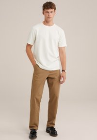 Fehér pamut póló rövid ujjakkal, barna chinos nadrággal és fekete bőr cipővel párosítva. Egyszerű design, semleges színek, mintázat nélkül.