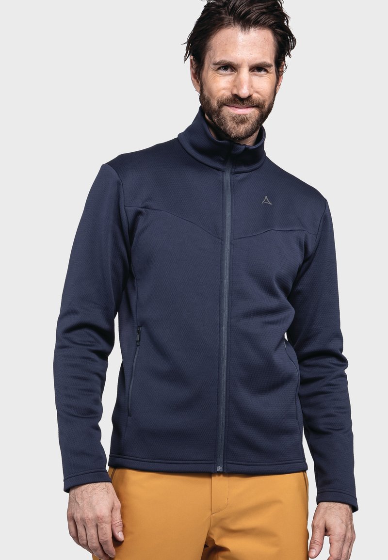 Marineblaues Fleecejacket mit hohem Kragen, strukturiertem Oberflächenmaterial, Frontreißverschluss und zwei seitlichen Taschen, kombiniert mit gelben Hosen.
