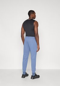 Μαύρη αμάνικη μπλούζα, ανοιχτό γαλάζιο παντελόνι φόρμας με μανσέτες και μαύρα παπούτσια. Λείος ύφασμα με ελαστική μέση, μινιμαλιστική σήμανση και άνετη εφαρμογή.