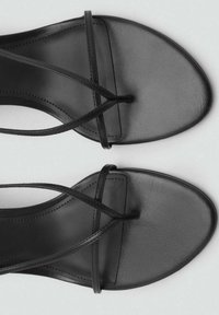 Schwarze flache Sandalen mit einem glatten Leder-Obermaterial, spitzem Zehenbereich und einem überkreuzten Riemendesign. Dezente Nähte betonen die Kanten.