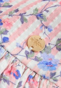 Povečava roza in bele tkanine s črtami ter modrim in roza cvetličnim potiskom, s majhnim okroglim zlatim gumbom z vgraviranim vzorcem.