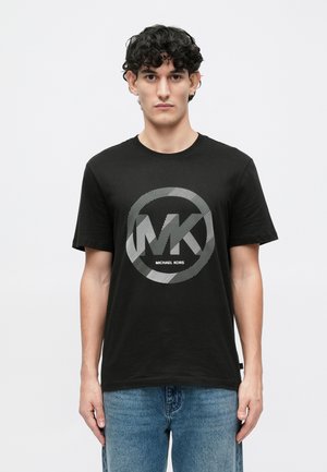 Musta puuvillane T-särk, millel on suur ümmargune graafiline kujundus, millel on valged tähed "MK" ja "MICHAEL KORS", lühikesed varrukad ja klassikaline ümar kaelus.