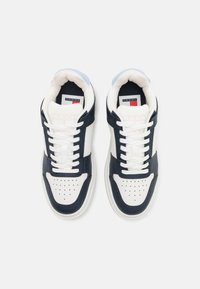 White and navy leather sneakers with rounded toe, perforated vamp, flat laces, and padded collar. Logo tag on tongue, rubber outsole.