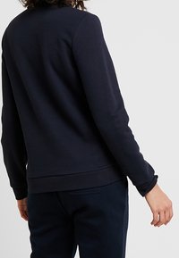Felpa navy con maniche lunghe, collo a giro, e polsini a costine. Presenta una texture liscia e una vestibilità comoda, mostrata dal retro.
