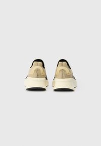 Sneakers ar beigtu sieta augšdaļu, melniem akcentiem un masīvu krēmkrāsas zoli. Aizmugures skats parāda noapaļotu papēdi un teksturētu apdari.
