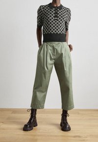 Czarny sweter polo z kremowym geometrycznym wzorem, krótkie rękawy, trzy guziki z przodu, połączony z zielonymi, luźnymi spodniami o wysokim stanie oraz czarnymi sznurowanymi butami.