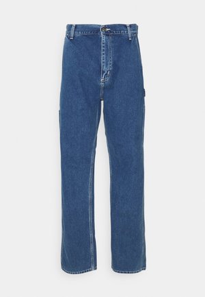 Jean denim bleu à jambe droite avec fermeture avant à boutons et fermeture éclair, passants de ceinture et poches latérales sur fond blanc.
