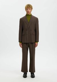 Pruuni kahekaraline ülikond laia säärega pükstega, mis on kombineeritud rohelise soonikkoega kõrge kaelusega särgiga. Kujundatud siledast kangast ja struktureeritud lõikega.