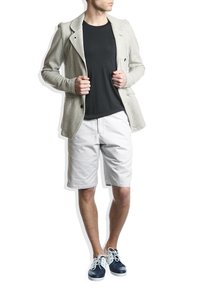 Blazer gris clair avec une finition texturée, porté sur un t-shirt noir. Associé à un short blanc et des baskets bleu marine avec des lacets blancs.