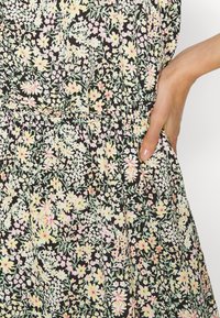 Vestido preto floral com pequenas flores rosa e amarelas, acompanhadas de folhas verdes. Tecido texturizado com cintura elástica e bolsos.