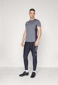 Grå sportstrøje med korte ærmer, parret med sorte, tætsiddende bukser med en sideløsning og logo. Fuldført med sorte løbesko.