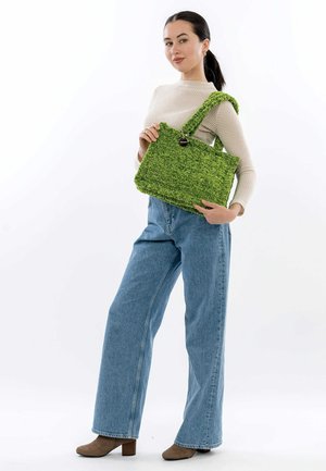 Grüne strukturierte Tragetasche mit einem robusten Design, ausgestattet mit einem langen Tragegurt und einem runden Hardware-Akzent. Getragen mit hellblauen weiten Jeans.