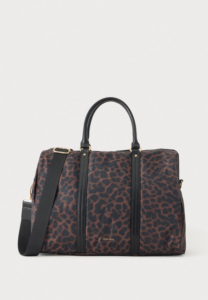 Grand sac de sport rectangulaire avec imprimé léopard noir et marron, anses noires, bandoulière réglable et quincaillerie dorée.