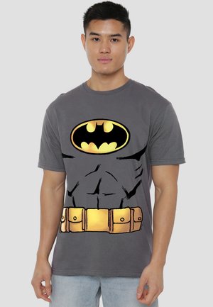 Young man wearing gray Batman-themed t-shirt with yellow and black logo, faux muscle print, and utility belt design.