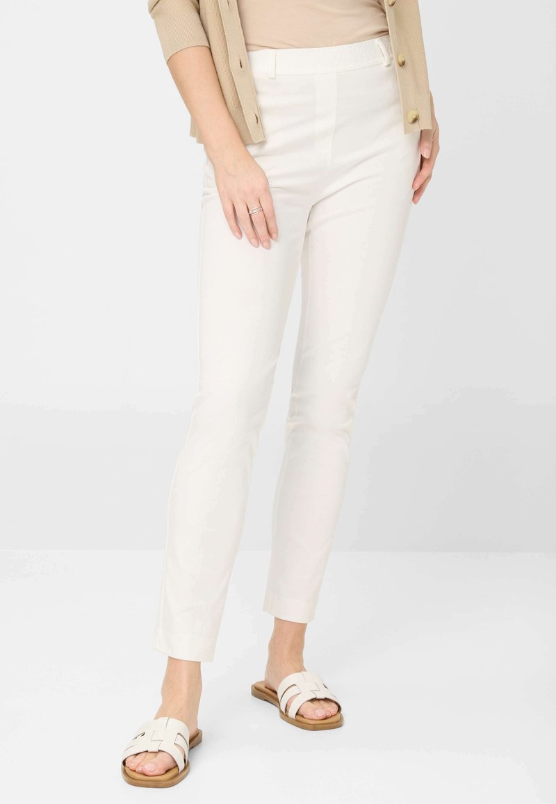 Pantalons blancs ajustés avec une texture lisse et une taille élastique, associés à des sandales à glissière beige clair avec un design de bride tissée.