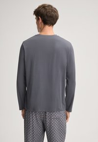 Langærmet grå skjorte med rund halslinje, glat tekstur og afslappet pasform, parret med mønstrede pyjamabukser.