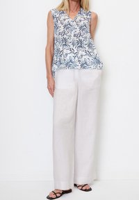 Blusa senza maniche in tessuto leggero, con un motivo floreale blu su sfondo bianco; abbinata a pantaloni in lino leggeri e svasati.