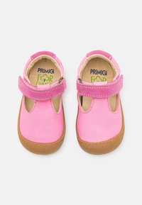 Vaaleanpunaiset nahka-vauvakengät, joissa on pyöreä kärki, säädettävä hihna ja ruskea kumipohja. Ominaisuuksiin kuuluvat leikattuja sivuja ja pehmeä vuori.