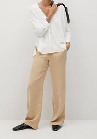 Blusa bianca a maniche lunghe con scollatura a V profonda, abbinata a pantaloni beige a gamba larga e mocassini neri, che trasmettono un comodo fitting e una texture morbida.