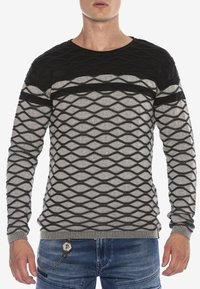Schwarzer und grauer Pullover mit einem strukturierten Design, das Diamantformen aufweist. Boots-Ausschnitt und gerippter Saum. Das Material scheint gestrickt zu sein.