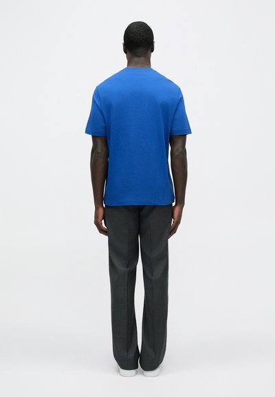 Modré tričko s krátkym rukávom a rovný strih, v kombinácii so sivými nohavicami zo mierne štruktúrovanej látky a bielymi teniskami.