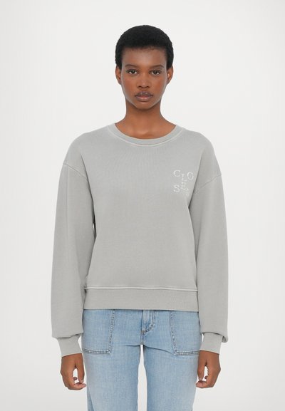 Gray sweatshirt with a crew neck and oversized fit, featuring a small "CLO" logo in white, paired with light blue jeans.