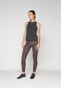 Débardeur de sport noir à sans manches, associé à un legging marron avec un motif noir ondulé et des chaussures de sport noires.