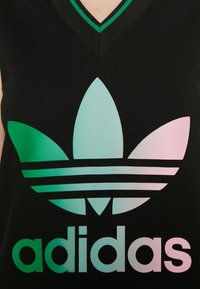 Débardeur noir avec un grand logo trefoil Adidas en dégradé pastel et du texte sur la poitrine, porté par une personne.