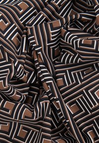 Kangas, jossa on geometrinen kuvio ruskeista, mustista ja valkoisista viivoista ja muodoista, näyttäen sileältä ja riippuvilta.