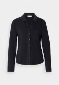 Chemise noire à manches longues avec boutons, col et poche poitrine, présentée sur un fond clair uni.