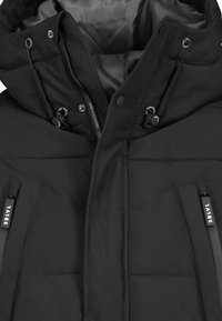 Schwarze isolierte Jacke mit Reißverschluss und Druckknopfverschluss, verstellbarem Kapuzen, und zwei seitlichen Taschen mit gebrandeten Reißverschlüssen. Glatte Textur.
