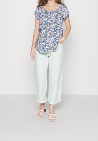 Top con motivo floreale nelle tonalità di blu, rosa e bianco, abbinato a pantaloni verdi menta chiari con risvolto e tacchi bianchi con cinturini.