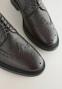 Chaussures brogue en cuir marron avec une finition texturée, un design à bout fleuri, des détails perforés et une semelle noire contrastante.