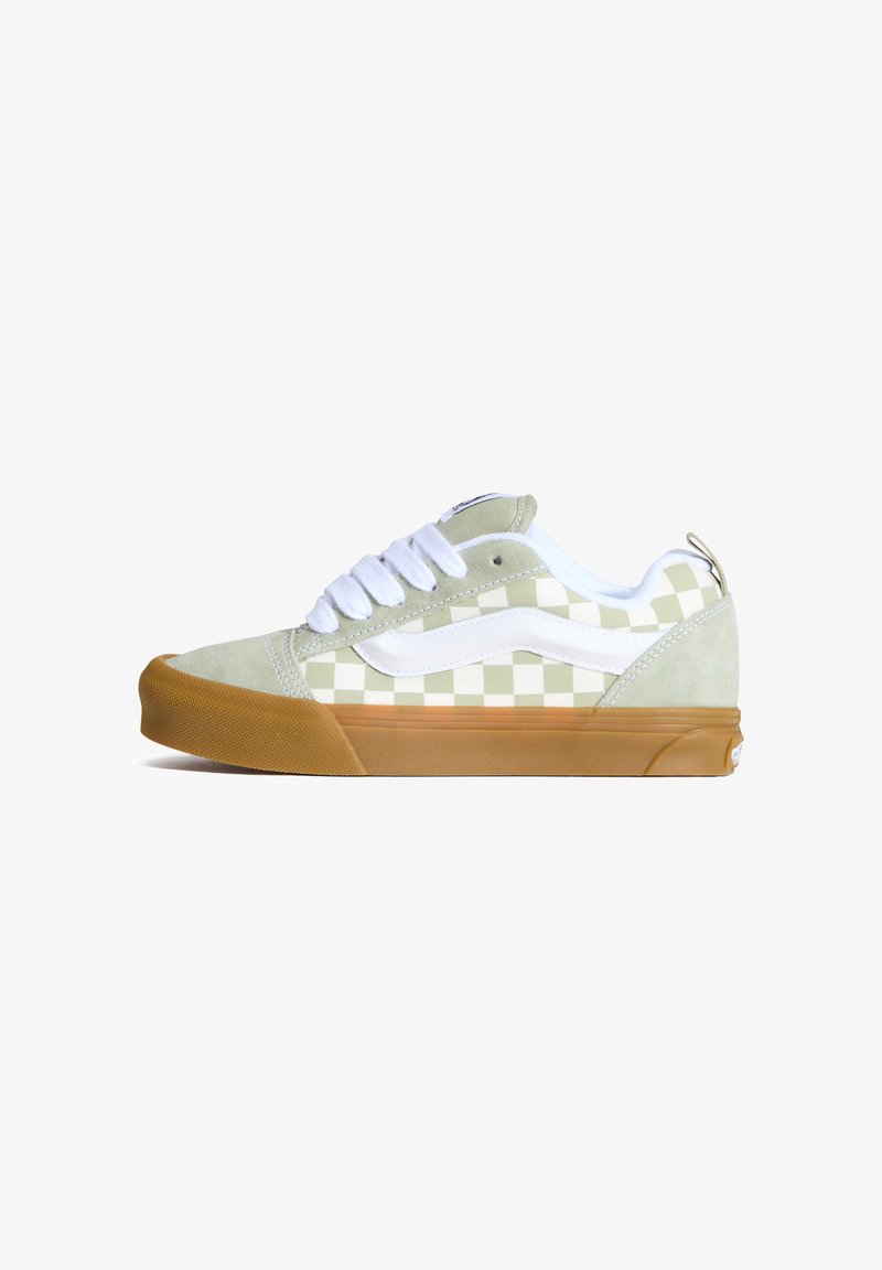 Chaussures de skate à damier vert et blanc avec une tige en daim, des lacets blancs et une semelle en caoutchouc marron clair. Vue de côté avec des détails de design distincts.