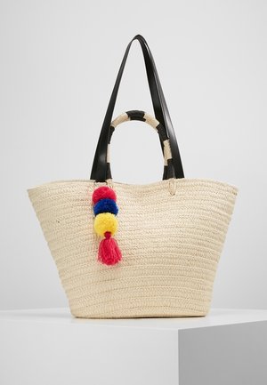 Woven straw tote bag in cream with black leather handles. Features multicolored pom-poms in red, blue, and yellow attached for detail.