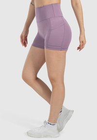 Pantalones cortos de talle alto en lavanda, elaborados con una tela elástica. Presentan detalles en las costuras y una textura suave, combinados con zapatillas deportivas blancas.