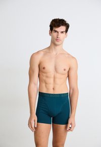 Boxer in teal con una morbida waistband elastica che presenta il logo "BJÖRN BORG" in verde scuro, progettati per una vestibilità aderente e comfort.