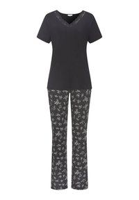 Melna V-veida krekls ar mežģīņu detaļām, savienots ar melnām biksēm ar baltu ziedu rakstu, veidojot kontrastējošu izskatu.