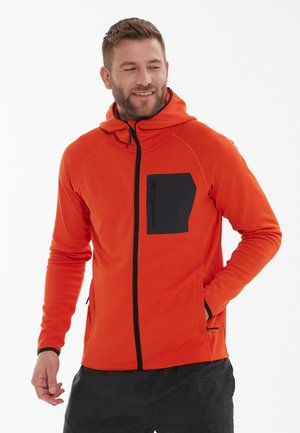 Rode hoodie van zachte stof, met een zwarte ritsborstzak en zwarte accenten. Rits aan de voorkant en kangoeroezakken aan de zijkanten.