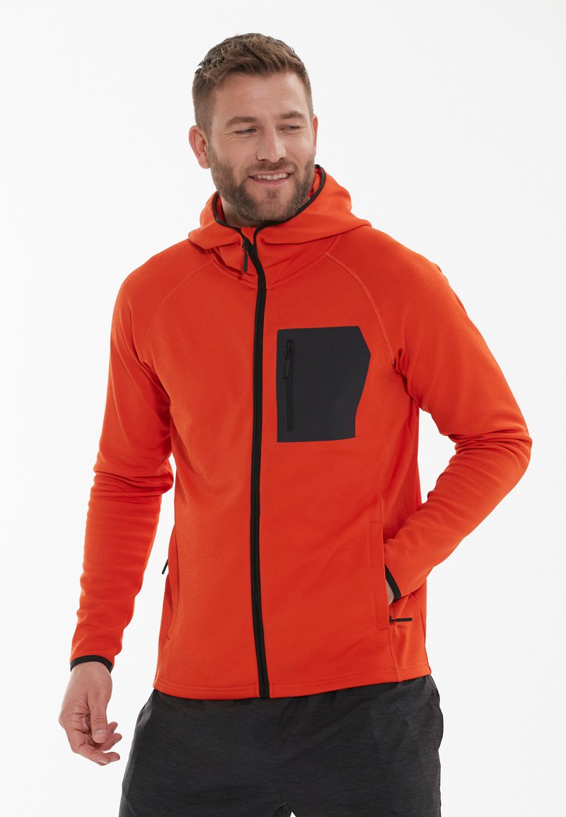 Rode hoodie van zachte stof, met een zwarte ritsborstzak en zwarte accenten. Rits aan de voorkant en kangoeroezakken aan de zijkanten.