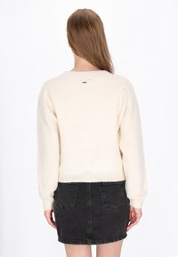 Crèmekleurige gebreide trui met een ribbeltextuur, ronde halslijn en verlaagde schouders, gecombineerd met een zwarte spijkerrok met zakken.