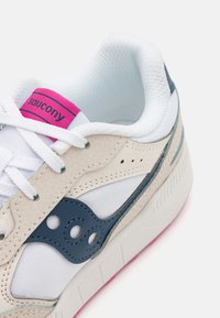 Baskets avec un dessus en maille blanche, des accents en cuir beige, un logo latéral bleu et une étiquette rose. Présente une semelle texturée avec un motif de bande de roulement.