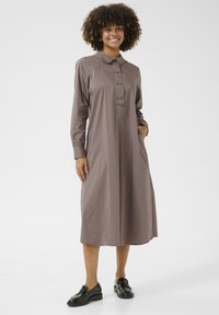 Rudos ilgomis rankovėmis suknelė su apykakle, mygtukų uždarymu ir kišenėmis. Slydus audinys, laisvas sijonas, siekiantis per vidurį blauzdų.