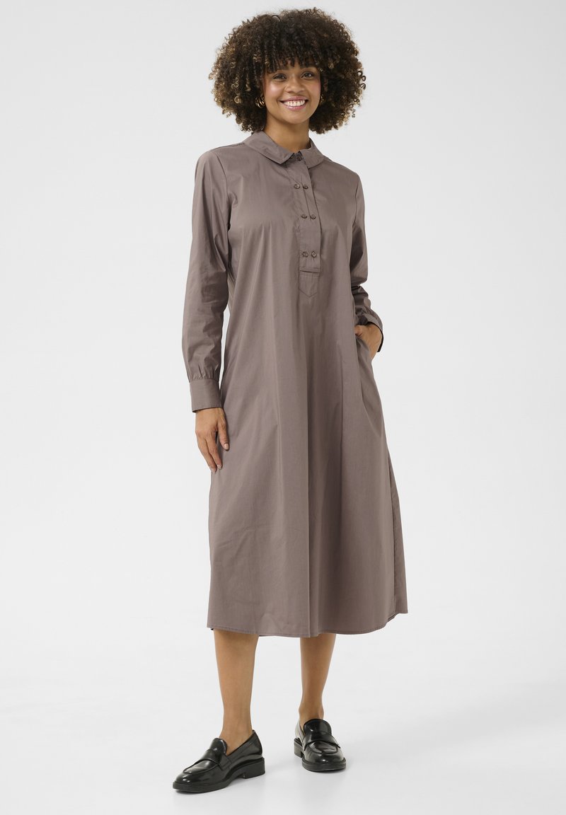 Rudos ilgomis rankovėmis suknelė su apykakle, mygtukų uždarymu ir kišenėmis. Slydus audinys, laisvas sijonas, siekiantis per vidurį blauzdų.