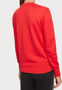 Röd sweatshirt med långa ärmar, rund hals, ribbade mudd och nederkant. Slät textur med en enkel design, inga synliga logotyper eller mönster.